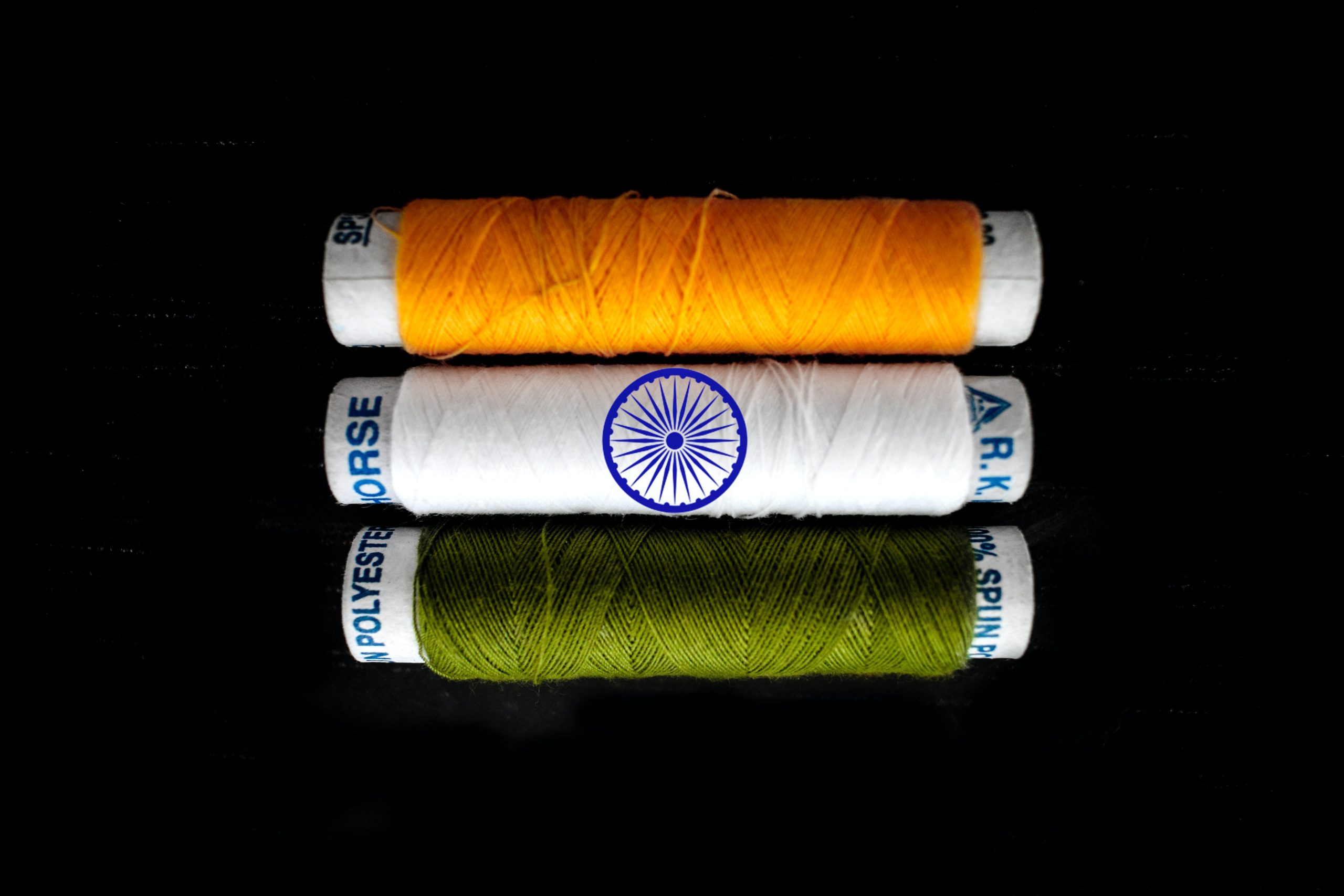 Photo of three spools of thread in orange, white, and green. Photo by Sikandar Ali via Unsplash.